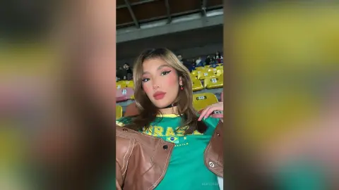 Stylish woman in a green Brazil jersey and brown leather jacket posing confidently at a stadium.