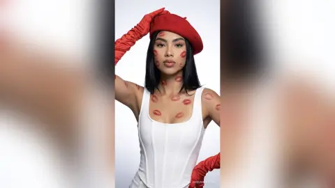 Fashionable woman in a white corset and red beret with red kiss marks on skin against a white studio background.