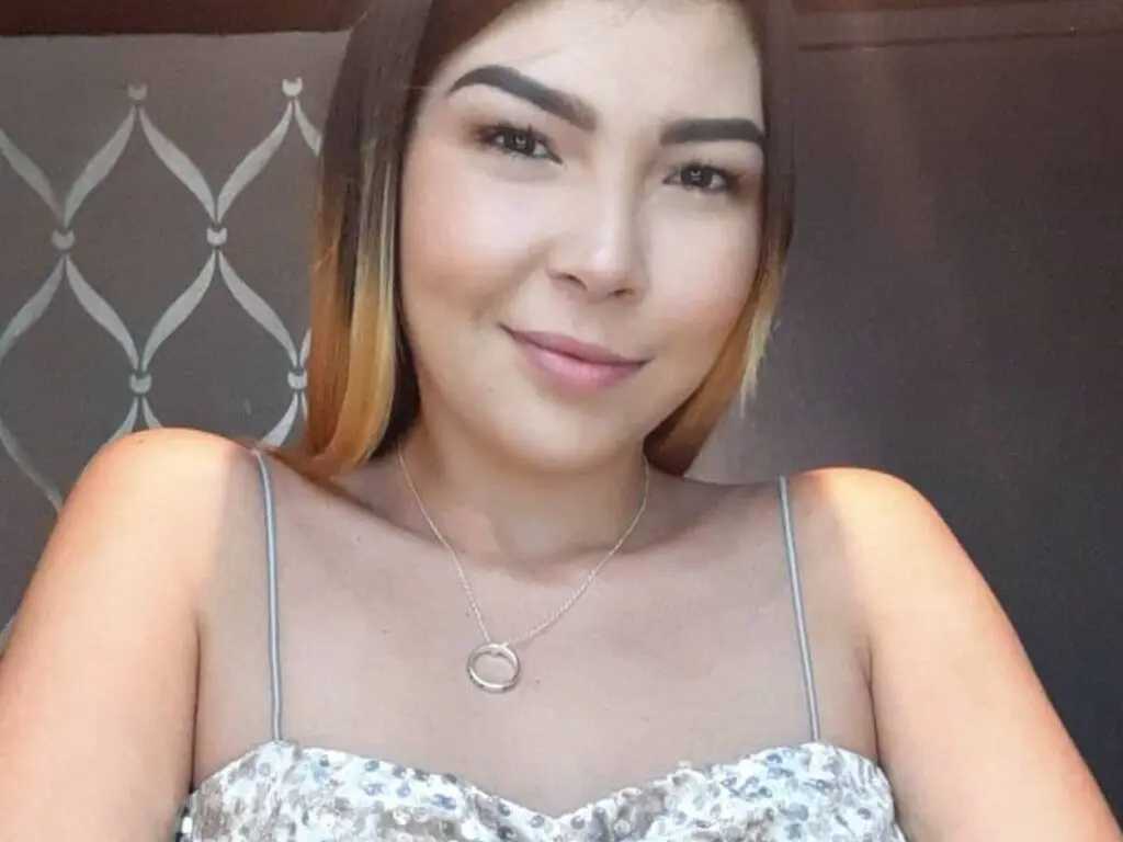 Smiling young woman in a silver sequin dress and silver necklace posing indoors with a soft glow.