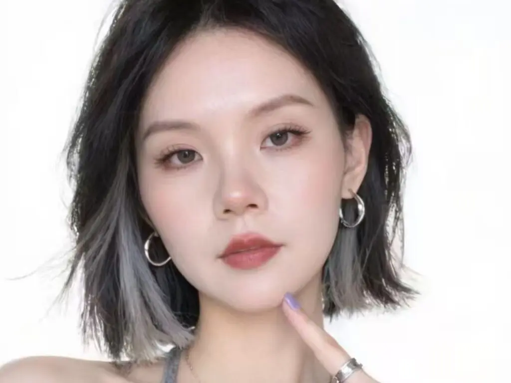 Young woman with short grey hair and silver hoop earrings posing against a white background.