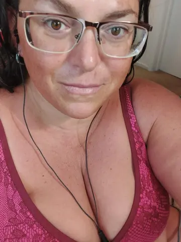 Smiling woman in a pink lace camisole wearing glasses in a bright indoor setting.