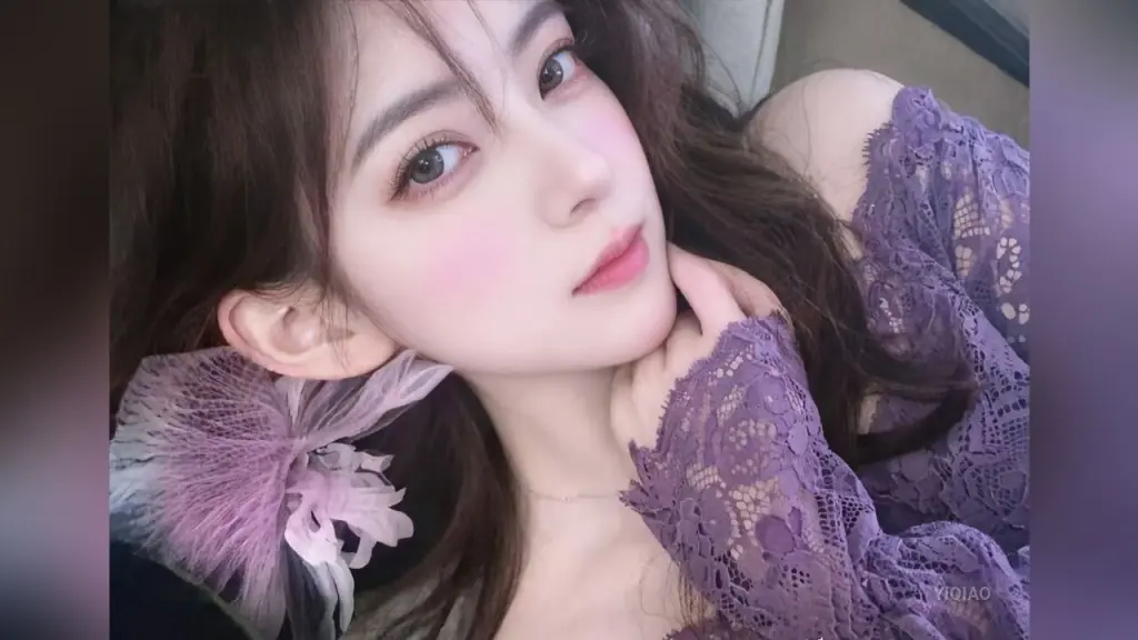 YiQiao — Young woman in a purple lace dress posing with a soft, romantic expression in a cozy indoor setting.