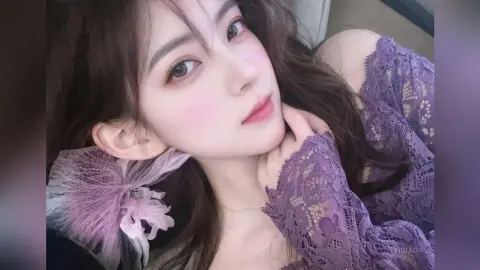 Young woman in a purple lace dress posing with a soft, romantic expression in a cozy indoor setting.