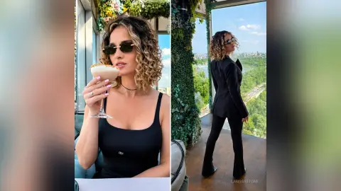 Stylish woman in a black tank top and sunglasses holding a cocktail on a sunny balcony.