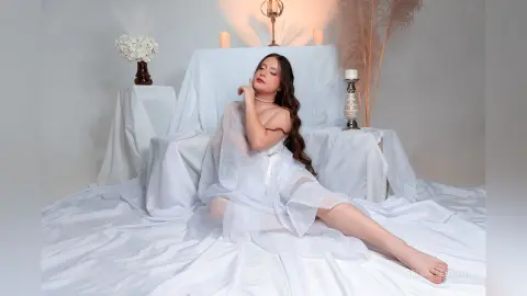 Elegant woman in a flowing white sheer dress posing in a dreamy, minimalist white studio setting.