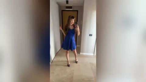 QuinnTakara poses in a blue dress for a mirror selfie in a hallway.