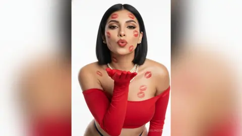 Glamorous woman in a red off-the-shoulder top blowing a kiss with red lipstick marks on her skin.