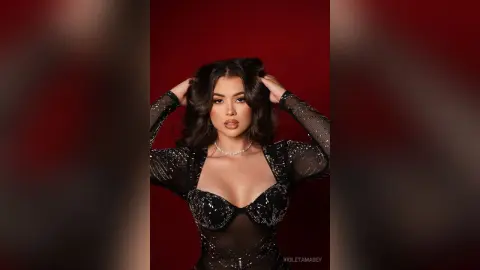 Glamorous woman in a sparkling black sheer bodysuit posing against a deep red background.