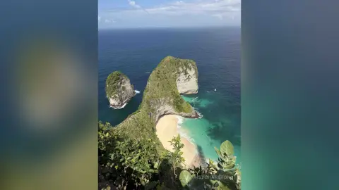 Aerial view of a tropical turquoise coastline with lush green cliffs and a secluded sandy beach under a clear sky.