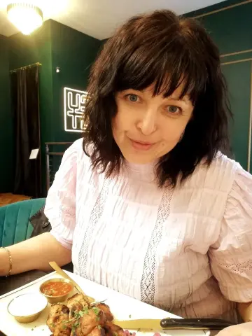 Polunichka039 with dark hair and a pink blouse sits at a table with a plate of food in front of her.