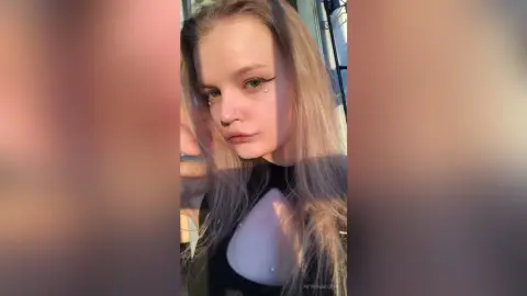 Blonde woman with winged eyeliner in a black cutout top posing in warm, cinematic sunlight.