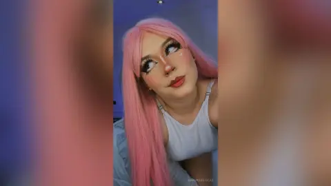 SakuraDilucas poses with long pink hair and heavy eyelashes, wearing a white tank top top.