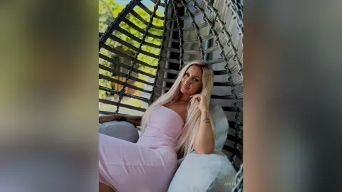 Anita poses in a light pink strapless dress while sitting in a hanging chair with her long blonde hair falling over her shoulder.