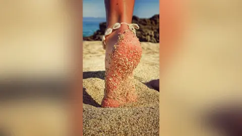 MarisaGrace's sandy foot resting on a beach with the ocean in the background.