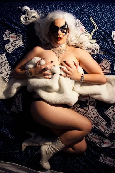 GayMerGeek poses in a red lace lingerie set, showing cleavage and her bare legs while sitting on a wooden floor.