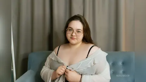 Smiling young woman with glasses in a white blouse sitting on a blue sofa in a cozy indoor setting.