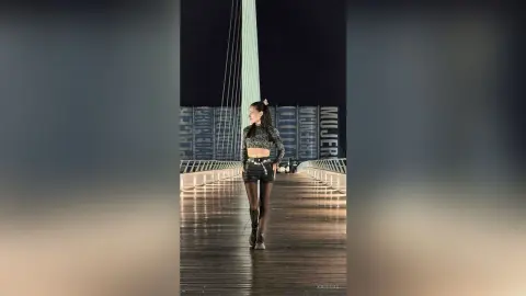 Stylish woman in a black crop top and denim shorts standing on a modern wooden pier at night.