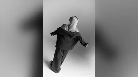 Elegant woman in black oversized shirt and wide-leg trousers posing gracefully in a minimalist studio setting.