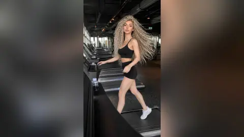 Athletic woman in black workout set walking on a treadmill in a modern, moody gym setting.