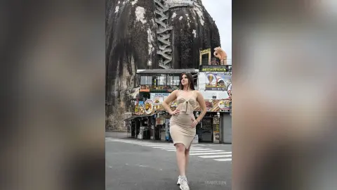 Woman in a beige midi dress posing in front of a restaurant near a massive rocky mountain cliff.