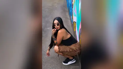 ChloeRiveiro — Stylish woman in black tank top and denim shorts posing in a colorful urban alleyway.