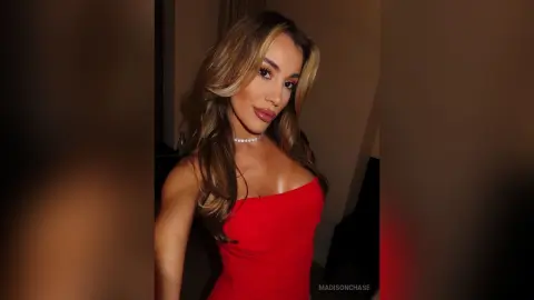 MadisonChase poses in a red dress and silver choker, showing off her long blonde hair and tan skin.