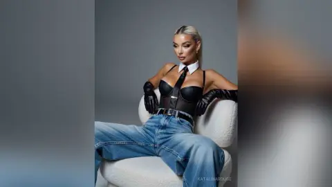 Fashionable woman in a black corset top, white collar, and blue jeans sitting in a studio setting.