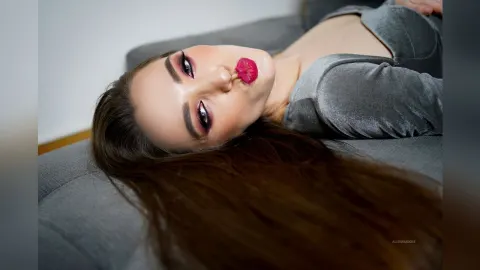 AlienaMoore — AlienaMoore lies on a grey sofa wearing a grey velvet top with her long brown hair spread out.