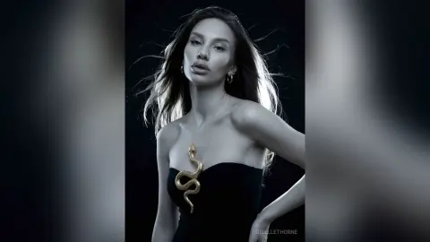 Elegant woman in a black strapless dress with a gold snake detail against a dark moody background.