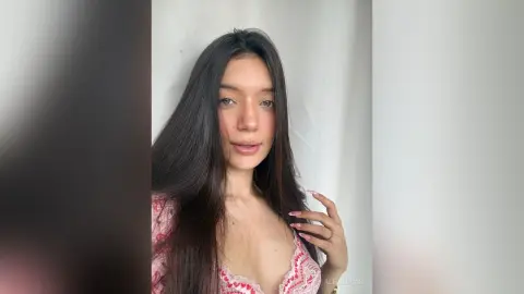 AleDilucas poses with her long dark hair down, wearing a pink and white lace top against a plain white background.