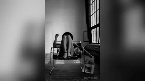LeslyAnderson reclines on a black chair, exposing her bare legs and feet in a black and white shot.