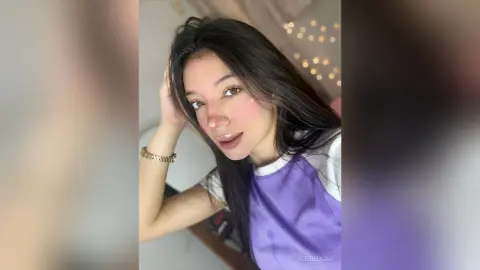 AleDilucas poses with her hand in her long black hair, wearing a purple and white t-shirt.
