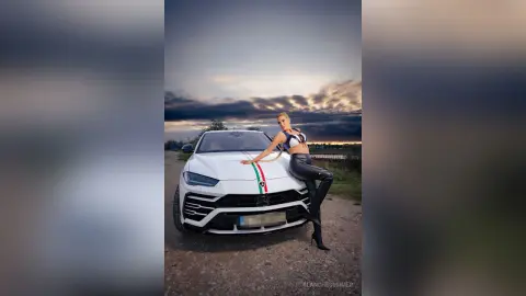 Stylish blonde woman in black leather pants leaning on a white luxury SUV during a moody sunset outdoors.