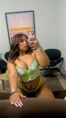 Curvy woman in floral lace lingerie set posing for a mirror selfie in a modern living room.