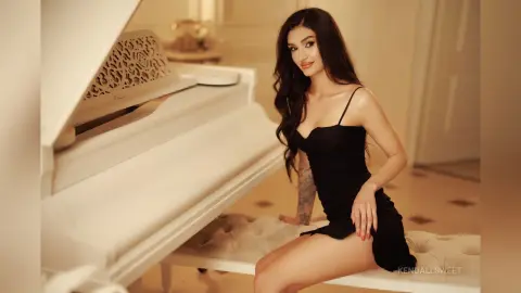 Elegant woman in a black slip dress sitting by a white grand piano in a bright, luxurious room.