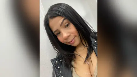 Smiling woman with long dark hair wearing a black leather jacket in a bright indoor setting.