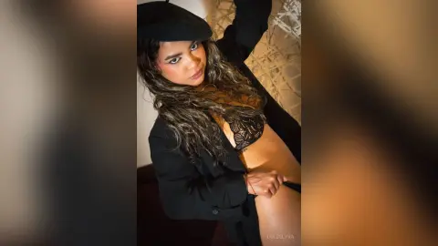 Glamorous woman in black lace lingerie and blazer posing with moody lighting in a stylish indoor setting.