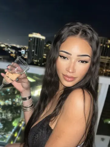 Glamorous woman in a black lace top holding a cocktail glass on a rooftop overlooking a city skyline at night.