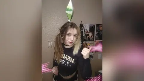 Young woman in a black graphic long-sleeve shirt posing indoors with a playful mood.