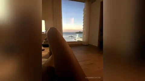 Relaxed view of legs resting by a window overlooking a calm ocean sunset from a luxury seaside villa.