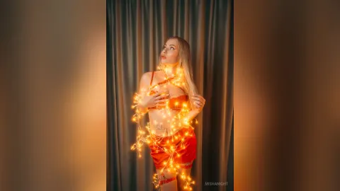 MishaNight — MishaNight poses in red lingerie wrapped in glowing orange fairy lights against dark curtains.