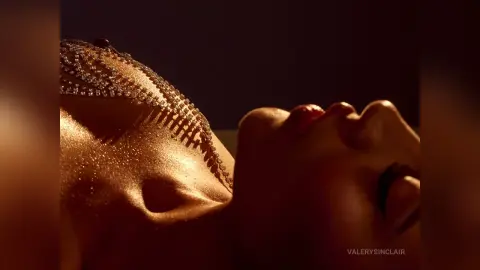 Glamorous woman in sparkling diamond jewelry lying in warm, dramatic lighting for a luxury beauty portrait.