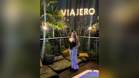 Smiling woman in a black tank top and light jeans relaxing on a lounge sofa at a tropical outdoor night lounge.