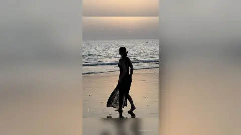LuanaRodgers walks along a beach at sunset wearing a long black dress.