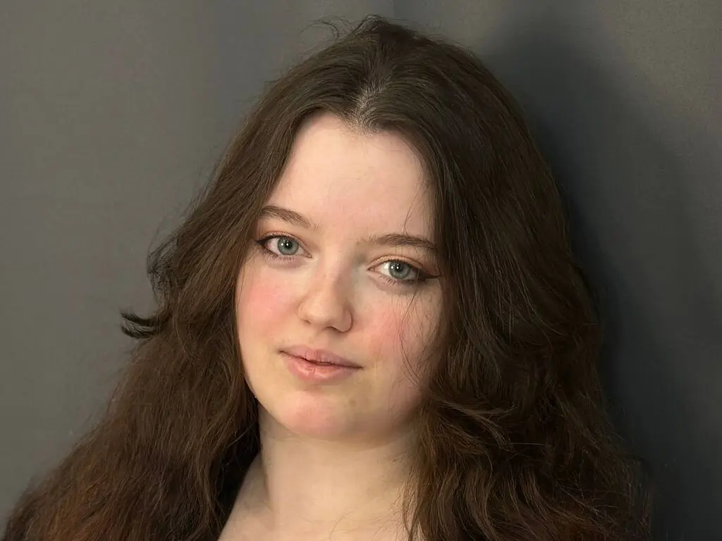 Portrait of a young woman with long wavy brown hair and natural makeup against a dark grey background.
