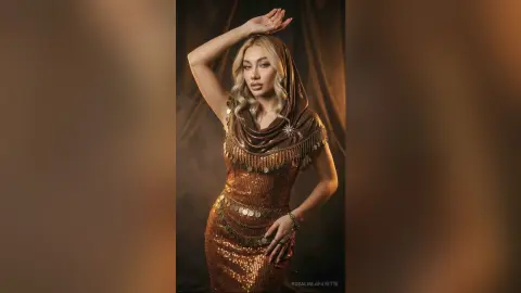Elegant woman in a shimmering bronze sequin gown and gold coin belt posing in a moody, dramatic studio setting.