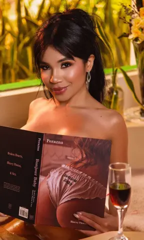 ArianaWoods smiles while holding a book titled Bonjour Baby in a warm, indoor setting.