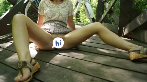 Woman in a lace top and floral skirt sitting on a wooden deck in a sunny forest setting.