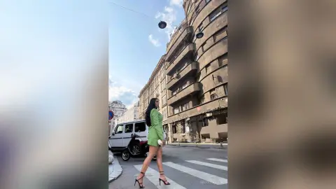 NicoleBella stands on a city street wearing a short lime green dress and black high heels.