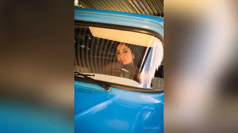 JuliahLewis looks through a car window, wearing a black top with her dark hair pulled back.